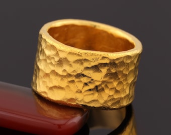 May include: A gold ring with a hammered texture. The ring is thick and has a wide band.