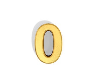 May include: A gold-colored number zero, with a textured surface, casting a shadow on a white background. The zero is an oval shape with a hollow center. The overall design is simple and elegant.