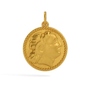 May include: A gold-colored pendant in the shape of a coin with a profile of a woman's face on one side. The coin has a beaded border.