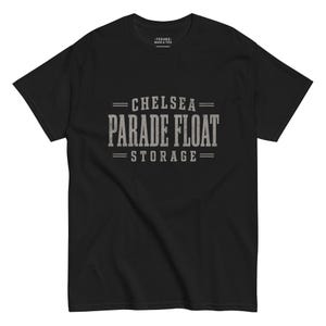 May include: A black short-sleeve t-shirt featuring the gray distressed text CHELSEA PARADE FLOAT STORAGE centered on the chest. The shirt has a crew neckline and a small interior neck label that reads TEEHEE MUGS & TEES in white text.