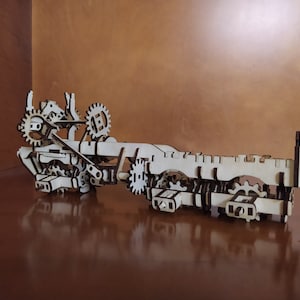 May include: A wooden model of a complex gear system with multiple interlocking gears and axles. The model is made of light brown wood and has a natural finish.