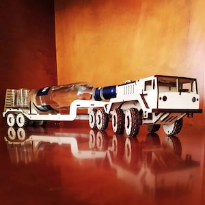 Puede incluir: Un modelo de madera de un camión transportando una botella de vino. El camión tiene seis ruedas y un remolque de plataforma. La botella es de vidrio transparente con una etiqueta azul.