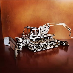 Può includere: Un modello in legno bianco di una macchina spazzaneve con un braccio sollevato e un aratro. Il modello è dettagliato con molte piccole parti.