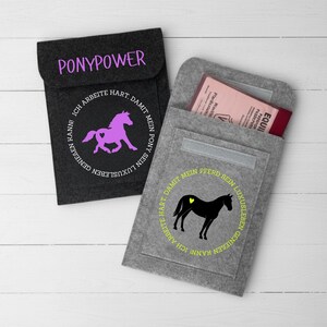 May include: Two felt passport holders. One is dark gray with the word "PONYPOWER" and a purple horse graphic. The other is light gray with a black horse graphic and text. Both have a flap closure.