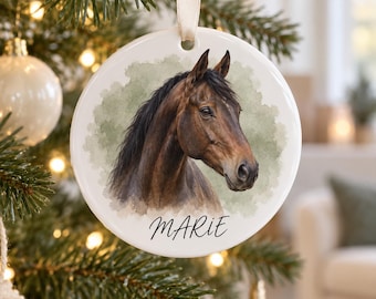 May include: A round white ceramic ornament featuring a detailed illustration of a brown horse head with a black mane against a soft green watercolor background. The name MARIE is printed in black script lettering at the bottom of the ornament.