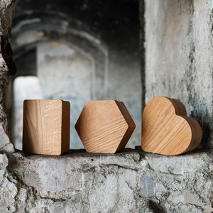 May include: Four wooden shapes, a square, a hexagon, a pentagon, and a heart, are arranged in a row on a weathered brick wall.