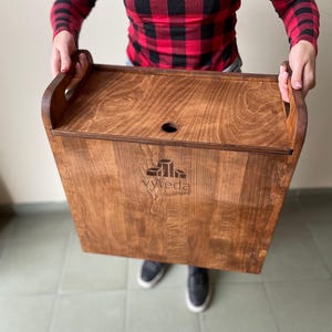 Op de afbeelding: Een rechthoekige houten opbergdoos met een donkerbruine gebeitste afwerking, voorzien van geïntegreerde handgrepen aan de zijkanten en een afneembaar deksel met een rond gat. Het voorpaneel toont een lasergravure met de tekst "vyteda".