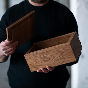 May include: A wooden box with a hinged lid, open to reveal the empty interior. The box is made of light brown wood with a natural grain pattern.