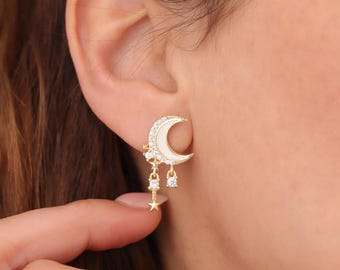 May include: Gold crescent moon earrings with white enamel and clear cubic zirconia stones. The earrings have a dangling star charm.