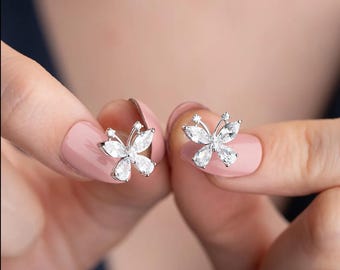 May include: A pair of silver butterfly earrings with clear cubic zirconia stones. The earrings are shown on a model's fingers.