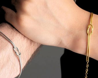 Puede incluir: Dos pulseras de nudo de oro, una con cadena y otra sin. Las pulseras están en las muñecas de dos personas.