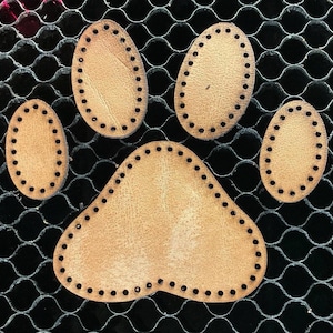 Könnte beinhalten: Fünf braune Leder-Pfotenabdrücke mit Nähten an den Rändern. Die Pfotenabdrücke befinden sich auf einem schwarzen Netz-Hintergrund.