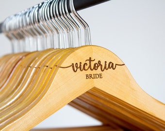 May include: A set of wooden hangers with a personalized inscription that reads "victoria BRIDE". The hangers are natural wood and have a satin finish.