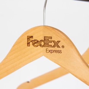 May include: Two wooden hangers with the FedEx Express logo engraved on the top. The hangers are light brown and have a silver hook.