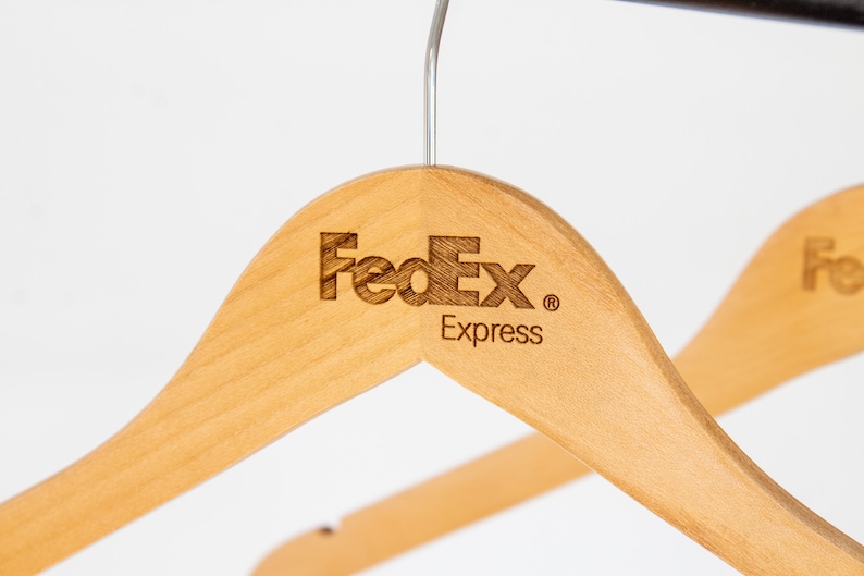 May include: Two wooden hangers with the FedEx Express logo engraved on the top. The hangers are light brown and have a silver hook.