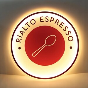 May include: Circular sign with the text "RIALTO ESPRESSO" in a curved font. The sign has a red center with a white spoon graphic. The outer ring is white with a warm, glowing light.
