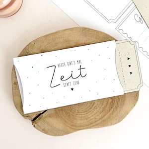 Könnte beinhalten: Eine weiße Geschenkkarte mit dem Text "Heute gibt's mal Zeit statt Zeug" in Schwarz, auf einer Holzscheibe. Die Karte ist Teil eines DIY-Drucksets, mit zusätzlichen Karten und Text sichtbar. Eine Kerze ist im Hintergrund.