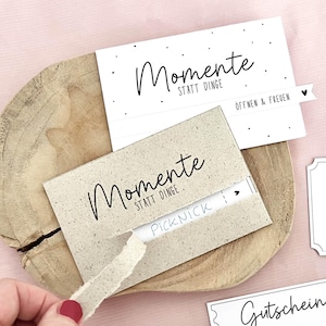Könnte beinhalten: Zwei Gutscheinkarten mit den Worten "Momente statt Dinge" in schwarzer Schrift. Eine Karte ist beige, die andere ist weiß. Das Bild enthält auch den Text "DIY Gutschein" und "PDF".