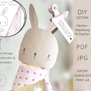 Peut inclure: Un emballage de bouteille de lapin de Pâques à faire soi-même. Le lapin est en papier brun clair avec des accents roses sur les joues et les oreilles. Il a une écharpe à pois roses et une étiquette avec "kleiner Ostergruß".
