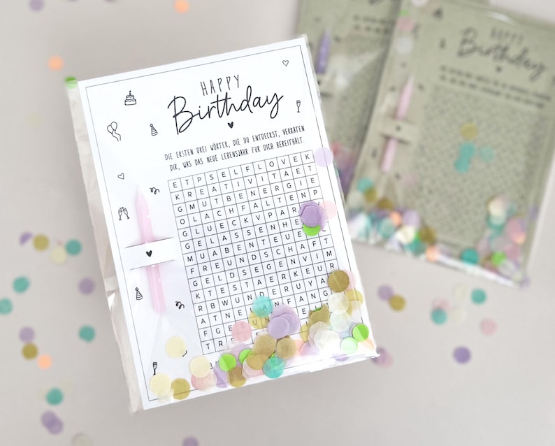 May include: A clear plastic bag containing a birthday-themed word search puzzle with the words "HAPPY Birthday" at the top. The bag also contains confetti and a pink candle. The background is white.