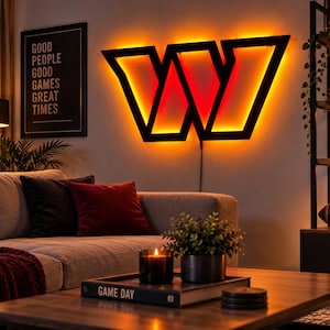 Pode incluir: Um grande letreiro de parede em forma de letra W, na cor preta, com retroiluminação LED laranja integrada. O design geométrico cria uma silhueta ousada e brilhante na parede, servindo como uma peça decorativa de destaque no ambiente.