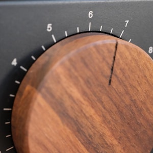 Peut inclure: Gros plan sur un cadran en bois sur fond noir. Le cadran est en bois brun foncé et comporte un trait noir indiquant le réglage. Des chiffres blancs de 3 à 8 sont visibles sur la surface noire, indiquant les réglages.