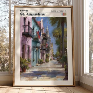 May include: Framed art print of St. Augustine, Florida. The artwork depicts a colorful street scene with buildings in shades of pink, blue, and green. Palm trees line the street, and the sky is a bright blue. The print includes the text "Florida St. Augustine".