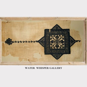 May include: A framed piece of fabric with a black and gold geometric design. The fabric is a light beige colour and the design is in the centre of the fabric. The frame is a light wood colour. The text "WATER WHISPER GALLERY" is below the frame.