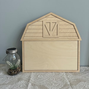 May include: A wooden barn-shaped sign with a blank chalkboard surface. The barn has a cutout door and a roof with horizontal planks.