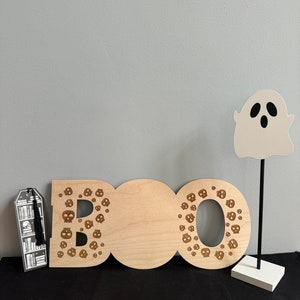 May include: Wooden BOO sign with a ghost cutout and a black tassel bookmark. The letters are decorated with small skull designs.