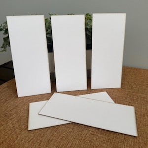 May include: A collection of blank, rectangular wooden signs. Three tall, vertical signs stand upright, while two smaller, horizontal signs are placed in front. The signs are white with natural wood edges, set on a brown surface.