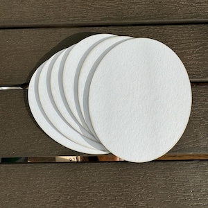 May include: A stack of six white round coasters made of felt.