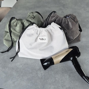 May include: Four drawstring bags made of corduroy fabric in green and brown colors. A white drawstring bag with the text "katr&agrave;" is in the center. A gold hairdryer is lying on the table.