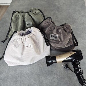 May include: Three drawstring bags made of corduroy fabric in green, brown, and white. The bags have a black drawstring and a label that says "katra". A black and gold hairdryer is also in the image.