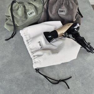 May include: Three drawstring bags made of corduroy fabric in green, gray, and white. The bags have the word "katra" printed on them. A hairdryer is inside the white bag.