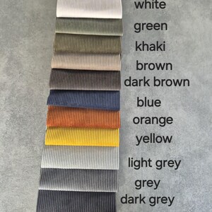 May include: A collection of 12 fabric swatches in various colors, including white, green, khaki, brown, dark brown, blue, orange, yellow, light grey, grey, and dark grey. The fabric is ribbed and has a textured appearance.
