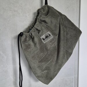 May include: A green corduroy drawstring bag with a black drawstring and a label that says "kaltra" hanging from a hook.