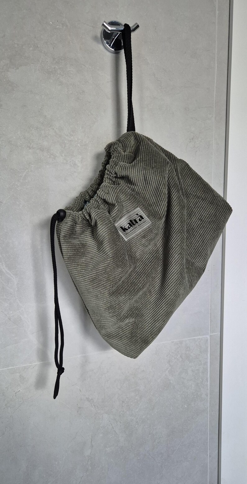 May include: A green corduroy drawstring bag with a black drawstring and a label that says "kaltra" hanging from a hook.