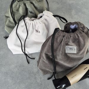 May include: Three drawstring bags made of corduroy fabric in green, white, and brown. The bags have a black drawstring and a small label with the word "kalt&auml;" on them.