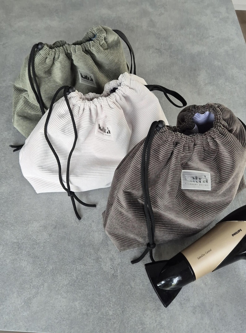 May include: Three drawstring bags made of corduroy fabric in green, white, and brown. The bags have a black drawstring and a small label with the word "kalt&auml;" on them.