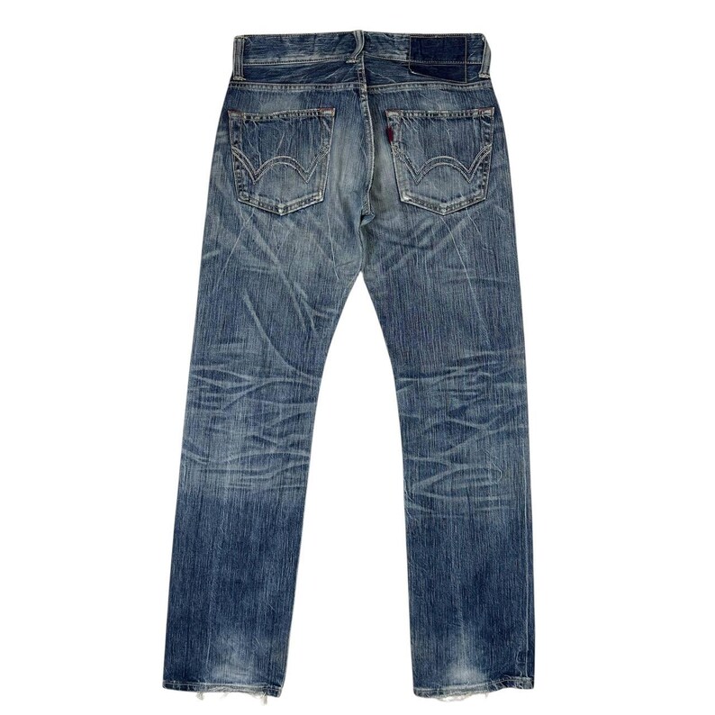 May include: Faded blue denim jeans with a classic five-pocket design. The jeans show signs of wear and tear, with distressed areas and a red tag on the back pocket. The back view highlights the stitching and the overall vintage aesthetic.