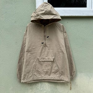 Puede incluir: Chaqueta anorak con capucha de color beige, con bolsillo frontal y cierre de media cremallera. La chaqueta tiene un cordón en el dobladillo y una capucha con cordón. Fabricada con tejido resistente, es adecuada para actividades al aire libre.