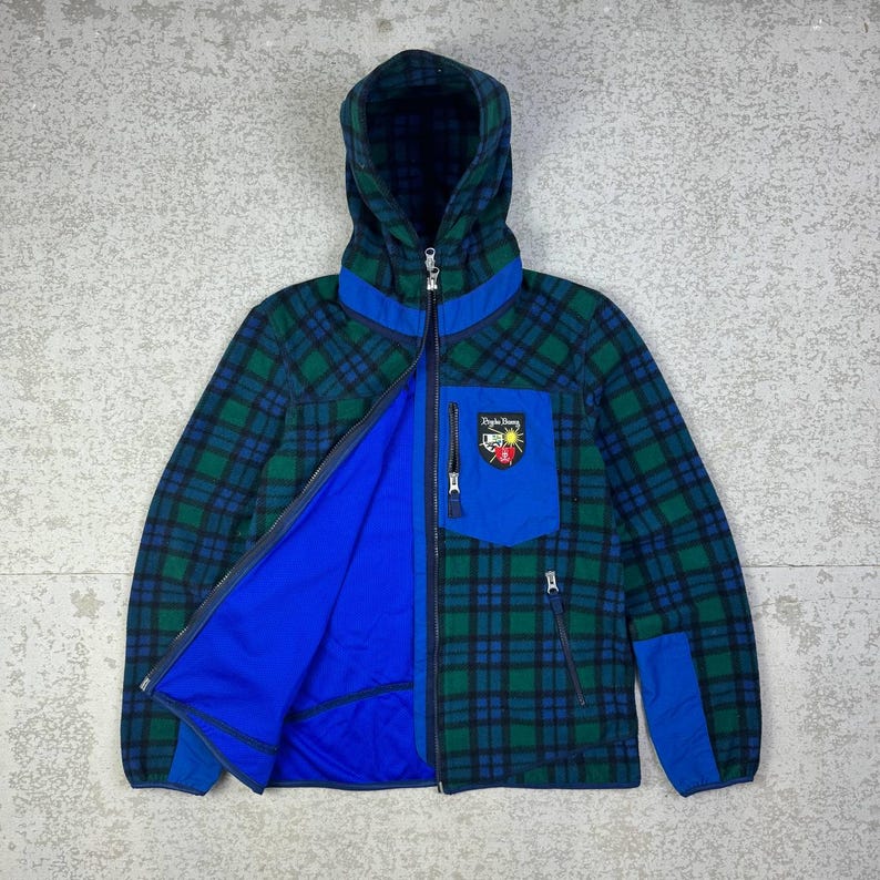 May include: A hooded jacket with a green and blue plaid pattern. The jacket has a blue interior, a blue pocket, and a zipper closure. A patch with text and a crest is on the pocket.
