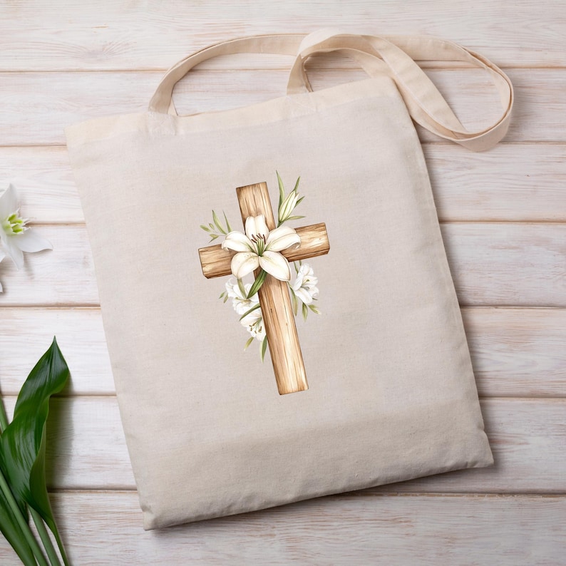 May include: Beige tote bag featuring a watercolor illustration of a wooden cross adorned with white lilies and greenery. The cross is centrally positioned, creating a religious or Easter theme. The bag has a simple design with a neutral color palette.