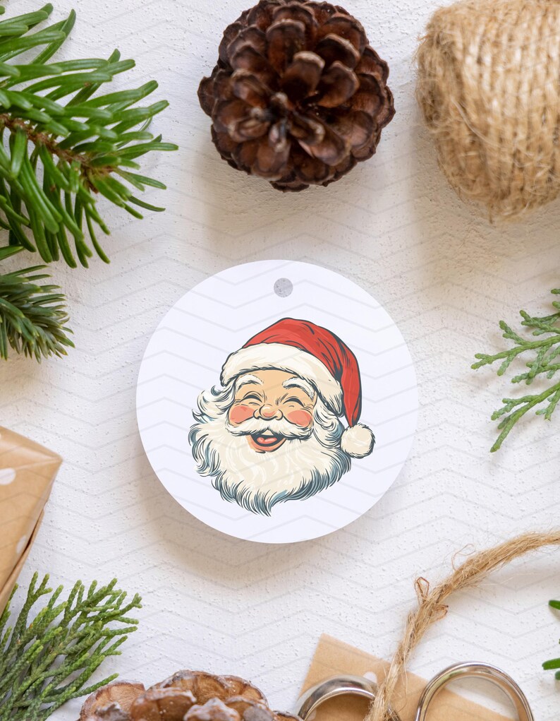 May include: A circular Christmas decoration with a smiling Santa Claus illustration. The design features a red hat, white beard, and rosy cheeks. The background includes festive elements like pine needles, a pine cone, and twine.
