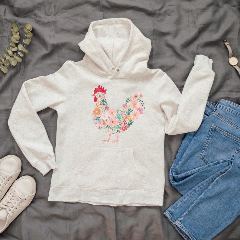 May include: A light gray hoodie with a floral rooster design. The rooster is composed of pink, yellow, and green flowers. The hoodie has a front pocket, a hood, and long sleeves. A pair of blue jeans and white sneakers are next to the hoodie.