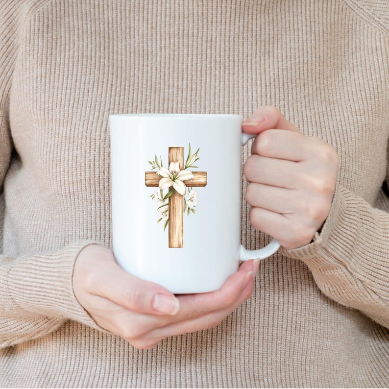 May include: White ceramic mug featuring a wooden cross design adorned with white lilies and green foliage. The cross is centered on the mug, creating a religious or Easter theme. The mug has a standard handle for easy gripping.