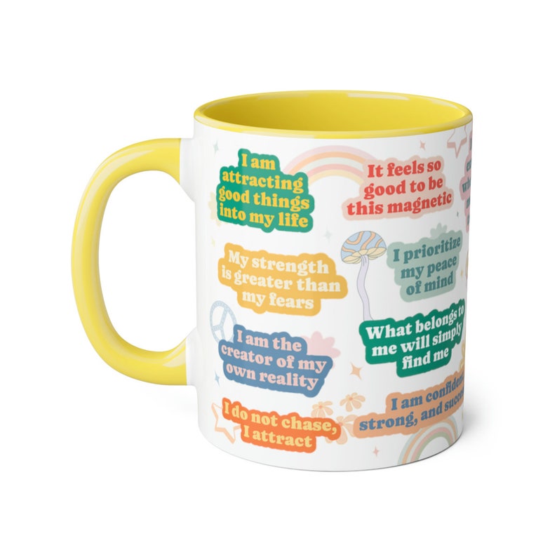 May include: White ceramic mug with a yellow interior and handle. The mug is decorated with colourful affirmations and a rainbow design. Text includes phrases like "I am attracting good things into my life."
