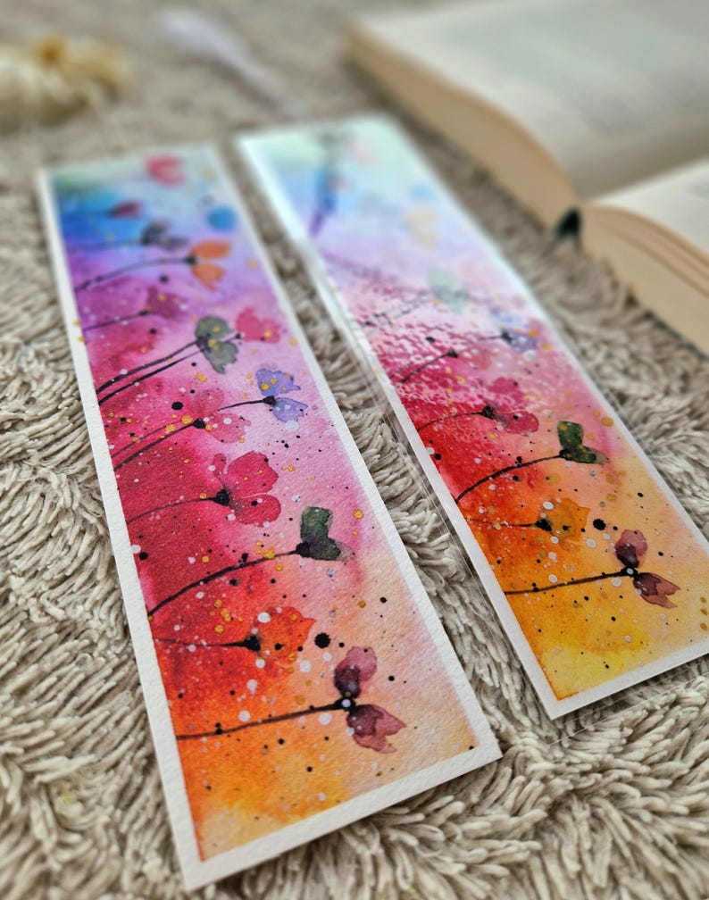 May include: Two watercolor bookmarks with a colorful floral design. The bookmarks feature a gradient background with red, orange, yellow, and blue hues. The flowers are painted in shades of pink, purple, and green. The bookmarks are perfect for adding a touch of color and whimsy to any book.