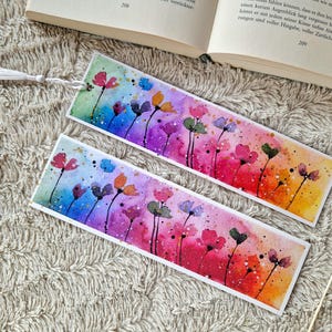 May include: Two watercolor bookmarks with a rainbow gradient background and colorful flowers. The bookmarks are white with a tassel.